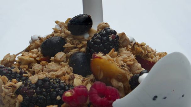 Verse melk gieten op sappige vruchten bessen met zoete granola op witte achtergrond close-up. Granenvlokken met frambozen bosbessen perzik bereiden met natuurlijke zuiveldrank. Gezond voedsel. - Foto, afbeelding