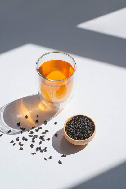 Китайский зеленый чай в деревянной чашке и стеклянной чашке. Сухие листья в контейнере на белом фоне. Органический высококачественный ингредиент для напитка - Фото, изображение
