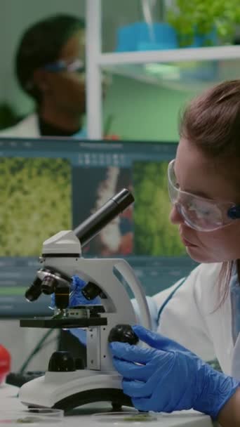 Vidéo verticale : Médecin scientifique analysant des plantes botaniques au microscope pour des tests chimiques. Biologiste chercheur spécialiste examinant la feuille de gomme organique tout en travaillant dans un laboratoire pharmaceutique - Séquence, vidéo