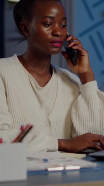Gece geç saatlerde dizüstü bilgisayarda çalışırken telefonda konuşan Afrikalı bir çalışan. İş için fazla mesai yapan serbest çalışan meşgul yazarlık, arama, finans projesinin son teslim tarihine saygı - Video, Çekim