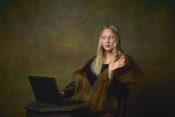Remote work. Shocked young charming girl in image of Mona Lisa, La Gioconda using laptop isolated on dark green background. Creative art, beauty, style, imitation, eras comparison - Foto, immagini