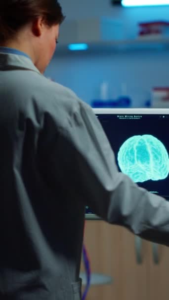Vertical video: Researcher looking at monitor analysing brain scan while coworker discussing with patient in background about side effects, mind functions, nervous system, tomography scan working in - Footage, Video