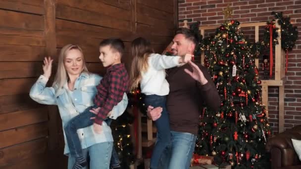 Γονείς που κρατούν τα παιδιά τους στα χέρια, χορεύουν μαζί κοντά στο Χριστουγεννιάτικο Δέντρο. Ευτυχισμένη ενεργή οικογένεια που χορεύει στο λαμπερό χριστουγεννιάτικο δέντρο σπίτι γιορτάζουν την παραμονή των Χριστουγέννων. Πρωτοχρονιά έννοια χειμερινές διακοπές - Πλάνα, βίντεο