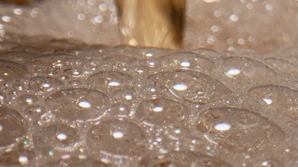 Schäumende Flüssigkeit Gießbehälter Nahaufnahme. Erfrischend sprudelnder Bierstrahl füllt transparentes Glas in Zeitlupe. Kohlensäurehaltiges Pils strömt und macht Mousse. Degustation alkoholische Getränke Konzept  - Foto, Bild