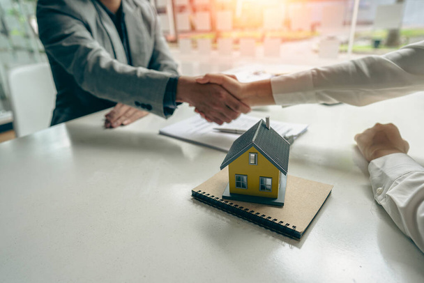 Ein Immobilienmakler schüttelt einem Kunden die Hand, nachdem er einen Vertrag zum Kauf oder zur Miete eines Hauses im Büro des Immobilienmaklers unterzeichnet hat. - Foto, Bild