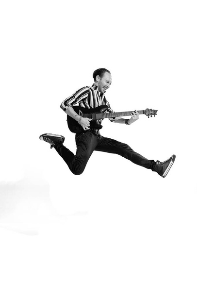 Portrait of young emotive man in stylish clothes playing guitar, posing isolated over white background. Black and white photo. Concept of music, rock and roll, lifestyle, fashion. Copy space for ad - Photo, Image