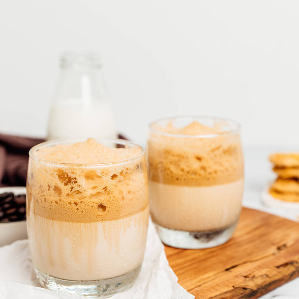 グラスカップやローストコーヒー豆にアイスコーヒーやフレップコーヒー、大理石を背景にミルク。テキストのスペースをコピー - 写真・画像