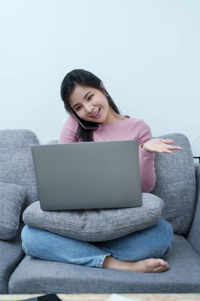 Muotokuva kaunis aasialainen teini tyttö käyttää puhelinta ja tietokonetta videoneuvottelut istuu sohvalla kotona. - Valokuva, kuva