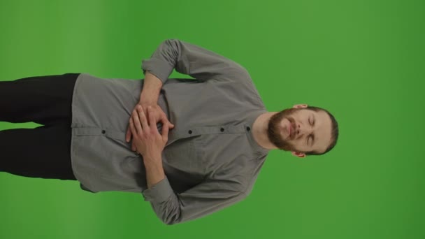 Vertikales Video, vertikale Ansicht. Schmerzhafter Krampf im Magen. Junger kranker, ungesunder bärtiger Mann umklammert Bauch und leidet unter starken Bauchschmerzen, Perioden von Krämpfen auf der grünen Leinwand, Chroma Key.Disease-Konzept - Filmmaterial, Video