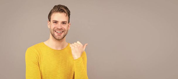 Reklama. Reklama. Šťastný chlap ukazuje prstem na šedé pozadí. Muž tvář portrét, prapor s kopírovacím prostorem - Fotografie, Obrázek