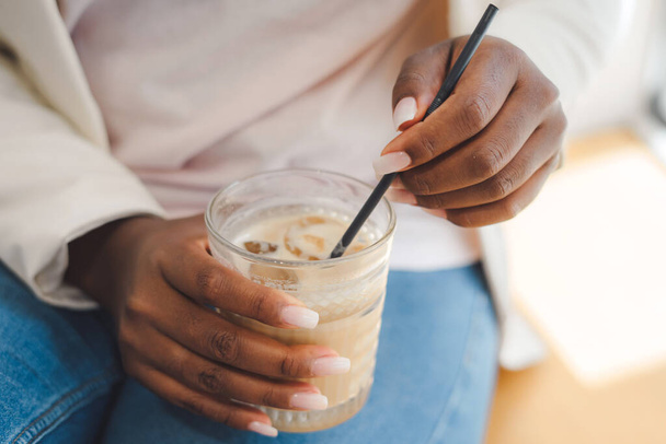 Een close-up van Afrikaans-Amerikaanse handen met een glas ijskoffie. Zomer hete zonnige dag. Mensen hun levensstijl. Moderne levensstijl. - Foto, afbeelding