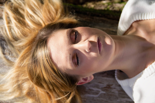 Portrait of young blonde caucasian woman laying on tree with closed eyes  - Foto, Imagen