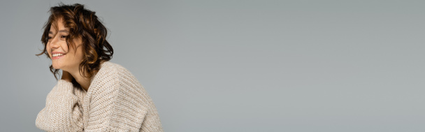 Nuori nainen aaltoilevat hiukset hymyillen neulottu villatakki eristetty harmaa, banneri - Valokuva, kuva