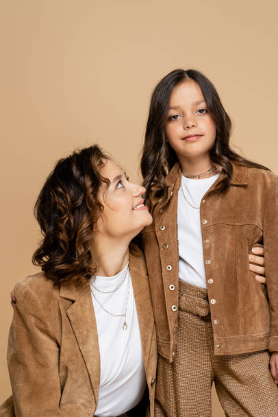 girl in stylish autumn jacket looking at camera near happy mom isolated on beige - Foto, imagen