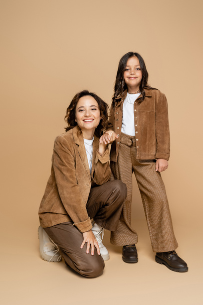 smiling mother and child in suede jackets and trendy clothes holding hands on beige background - Foto, Imagem