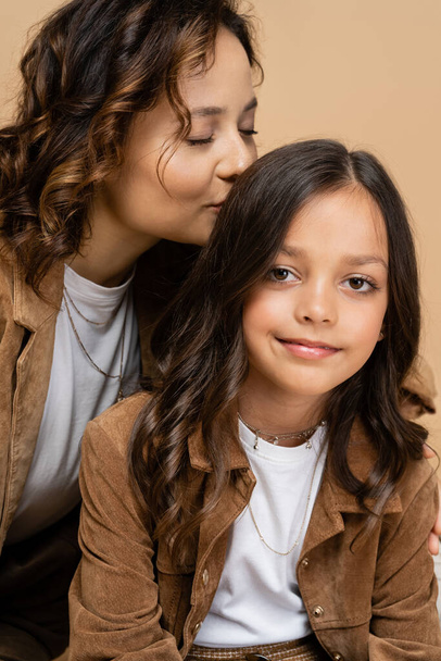 happy woman with closed eyes kissing hair of trendy daughter smiling at camera isolated on beige - 写真・画像