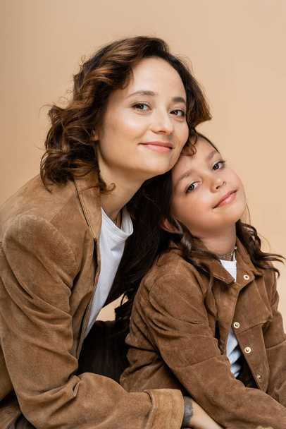brunette woman and girl in stylish autumn jackets smiling at camera isolated on beige - Photo, Image