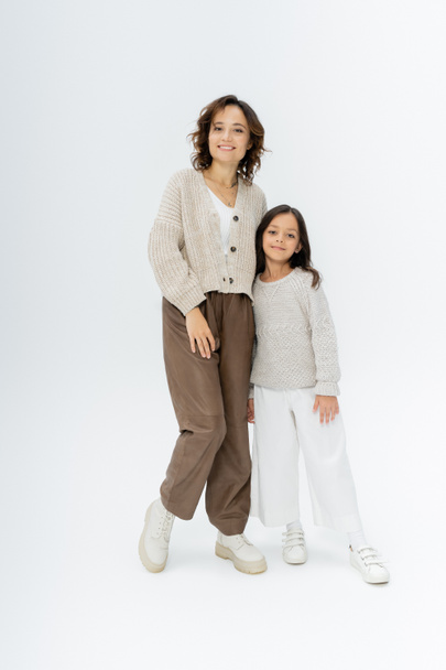 full length of mother and daughter in knitwear and pants posing on grey background - Photo, Image