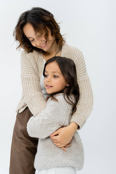happy brunette woman with daughter in warm knitwear embracing isolated on grey - Фото, зображення