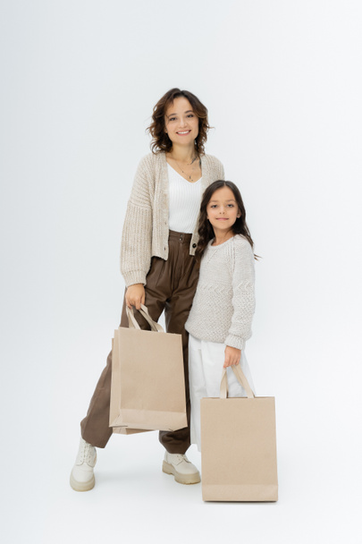 nő és lány divatos őszi ruhák gazdaság bevásárló táskák és nézi kamera szürke háttér - Fotó, kép