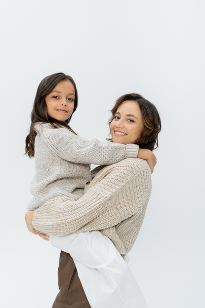 smiling woman and girl in knitwear embracing and smiling at camera isolated on grey - 写真・画像