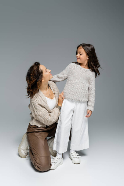 woman and girl in knitwear and trendy pants looking at each other on grey background - Photo, Image