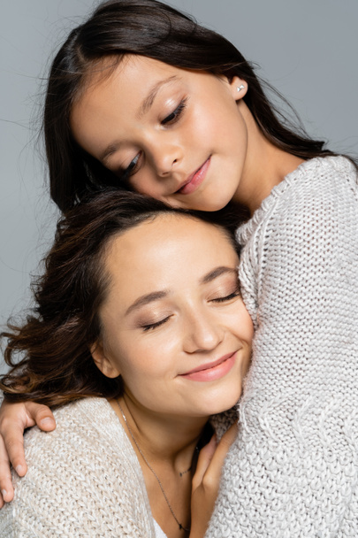 brunette girl embracing mother smiling with closed eyes isolated on grey  - 写真・画像