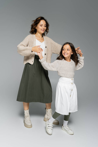 full length of woman and girl in skirts holding hands and dancing on grey background - Foto, imagen
