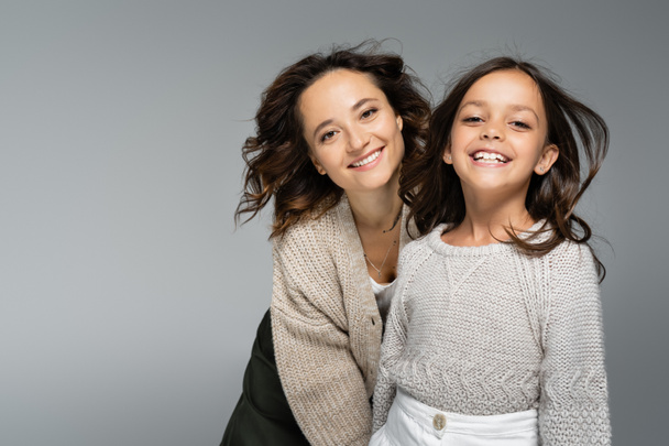 excited woman and girl in trendy autumn knitwear smiling at camera isolated on grey - Photo, image