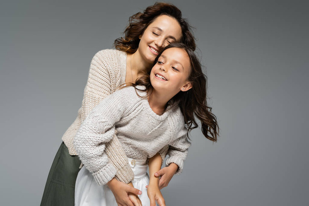 happy woman with closed eyes hugging daughter in warm knitwear isolated on grey - Foto, immagini