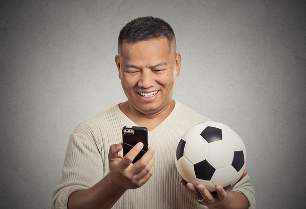 smiling surprised man looking on smartphone watching game holding football  - 写真・画像