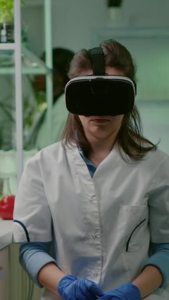 Pionowe wideo: Naukowiec kobieta naukowiec noszący wirtualną rzeczywistość gogle rozwija nową biotechnologię dla biologicznego eksperymentu. Zespół medyczny pracujący w laboratorium mikrobiologicznym analizującym test DNA - Materiał filmowy, wideo