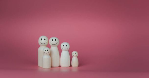 Happy house concept. Wooden dolls stand lined up against a pink background. Indicates happiness and love in the house. - Foto, Imagen
