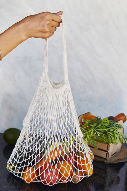 Woman holds eco shopping reusable bag full of fresh vegetables - tomatoes, purple potatoes, eggplants, carrots, sweet pepper. Ecological concern, eco shopping. Vegan eco-friendly lifestyle. - 写真・画像
