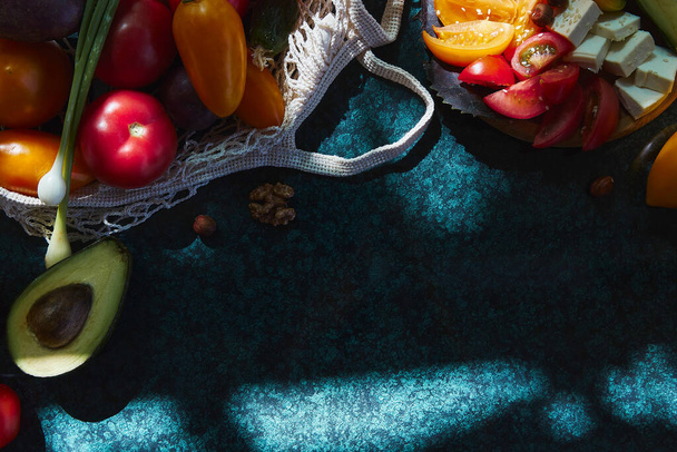Verduras - cebolla, tomates amarillos, remolacha y aguacate en bolsa ecológica bajo las sombras duras de moda con fondo de reflexión. Ensalada fresca de verduras. Comida saludable. Comida vista superior - Foto, Imagen