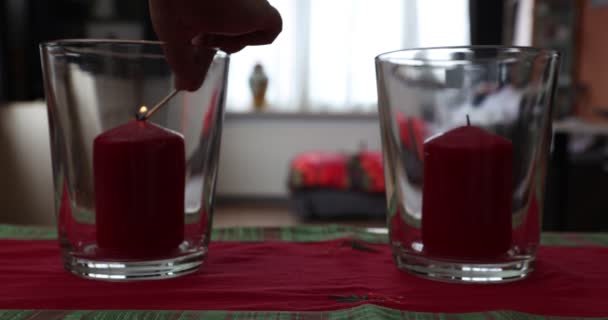 Erwachsene weibliche Hände zünden zwei rote Kerzen in Glaskerzenständern an und vermitteln ein Gefühl von Ruhe und Frieden im Wohnzimmer, Fenster vor verschwommenem Hintergrund. Konzept von Glaube und Hoffnung - Filmmaterial, Video