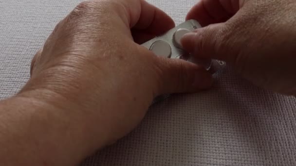 Mãos femininas de uma mulher idosa tomando dois comprimidos de paracetamol para aliviar uma dor de cabeça causada pela gripe, fundo branco. Conceito de grandes despesas com serviços de saúde - Filmagem, Vídeo