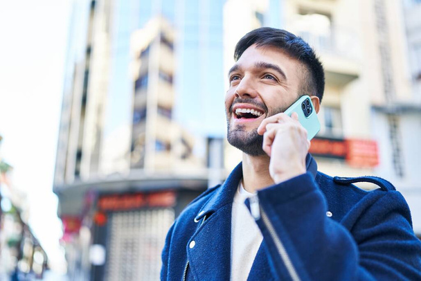 Молодий іспаномовний чоловік посміхається впевнено говорити по смартфону на вулиці
 - Фото, зображення