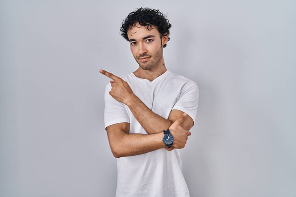 Ισπανόφωνος άνθρωπος στέκεται πάνω από απομονωμένη φόντο δείχνοντας με το χέρι δάχτυλο στο πλάι δείχνει διαφήμιση, σοβαρή και ήρεμη πρόσωπο  - Φωτογραφία, εικόνα