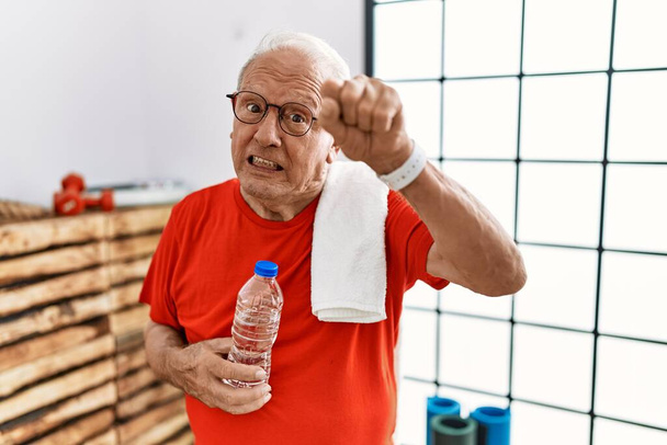 Starszy mężczyzna ubrany w odzież sportową i ręcznik na siłowni wściekły i wściekły podnoszący pięść sfrustrowany i wściekły krzycząc ze złości. wściekłość i agresywne pojęcie.  - Zdjęcie, obraz