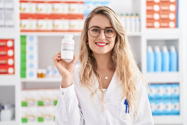 Jonge vrouw apotheker holding pillen fles bij apotheek - Foto, afbeelding