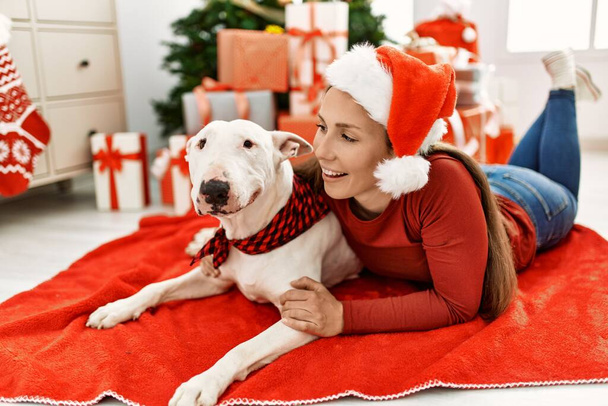 Nuori valkoihoinen nainen hymyilee luottavainen halaava koira makaa joulukuusi kotona - Valokuva, kuva