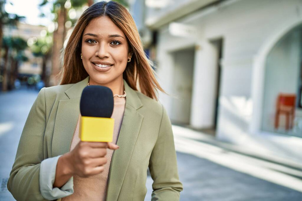 Giovane donna latina sorridente fiducioso utilizzando il microfono in strada - Foto, immagini
