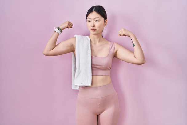 Čínská mladá žena na sobě sportovní oblečení a ručník ukazující paže svaly usmívající se hrdě. fitness koncept.  - Fotografie, Obrázek