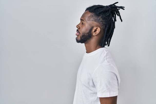 Homem africano com dreadlocks vestindo t-shirt casual sobre fundo branco olhando para o lado, relaxar pose perfil com rosto natural com sorriso confiante.  - Foto, Imagem