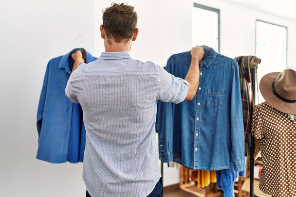 Молодий іспаномовний клієнт чоловік на задньому плані вибирає сорочку в магазині одягу
. - Фото, зображення