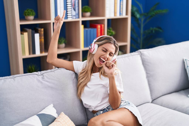 Young blonde woman listening to music singing song at home - 写真・画像