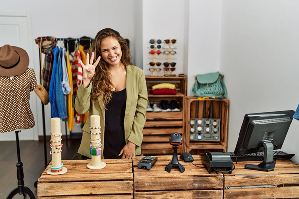 Красива іспаномовна жінка працює в модному магазині, показуючи і вказуючи пальцями номер чотири, посміхаючись впевнено і щасливо
.  - Фото, зображення