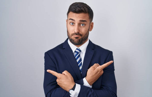 Handsome hispanic man wearing suit and tie pointing to both sides with fingers, different direction disagree  - Foto, afbeelding
