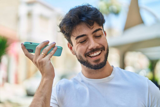 Jeune homme hispanique souriant confiant écoute message audio par le smartphone à la rue - Photo, image